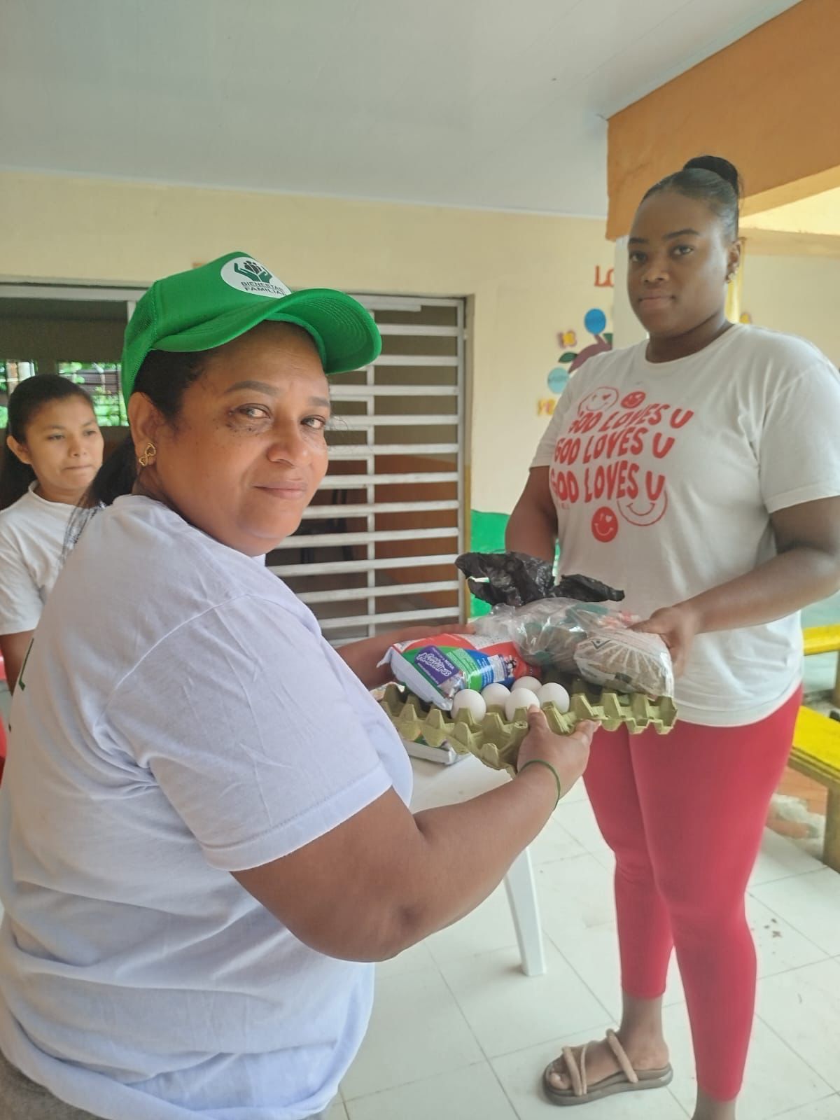 Beneficiaria del programa alimentario de Manos Amigas recibiendo canasta con huevos y alimentos en punto de distribución comunitario