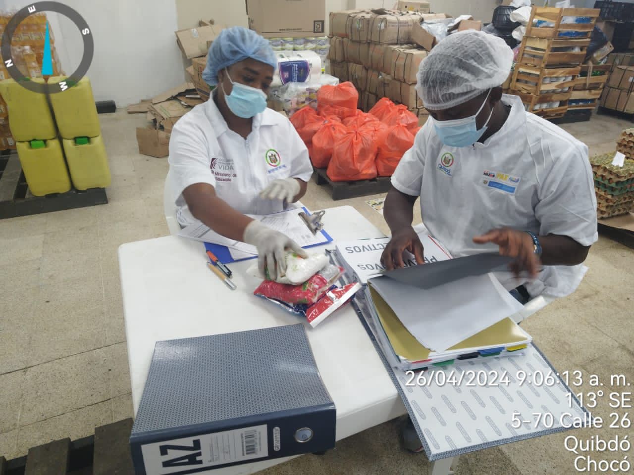 Dos profesionales de Manos Amigas con tapabocas y gorros revisando documentación e insumos alimentarios en bodega de Quibdó